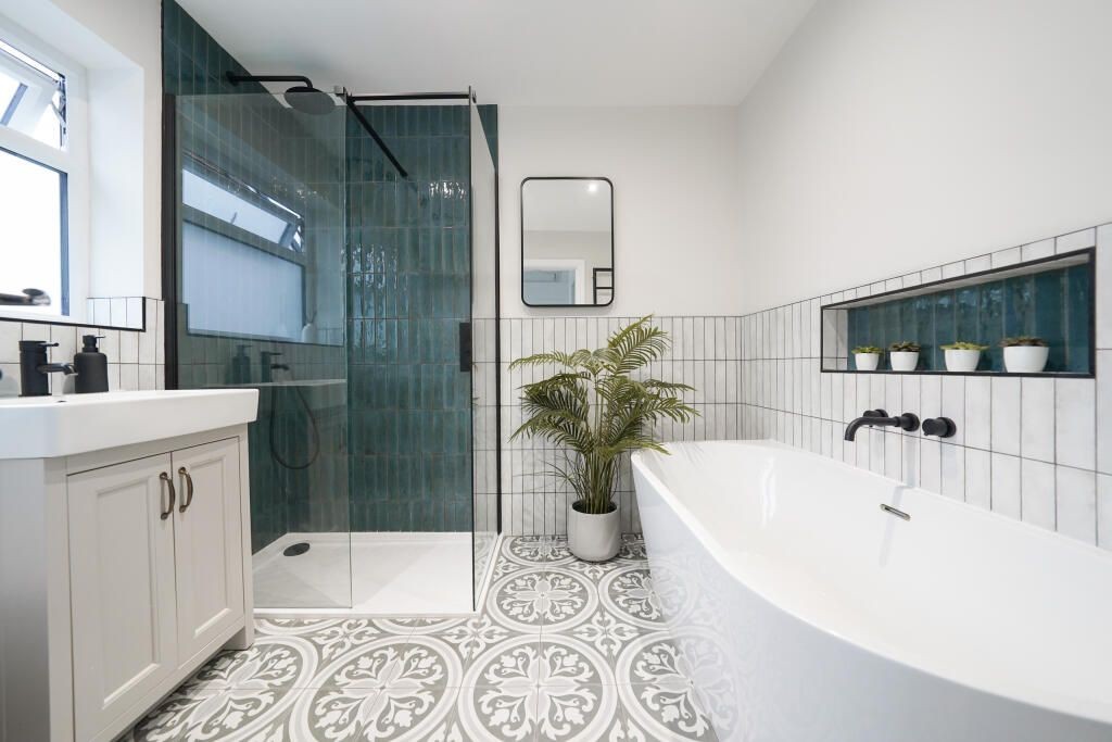 Modern bathroom featuring a glass shower, bathtub, potted plant, and stylish patterned floor tiles.